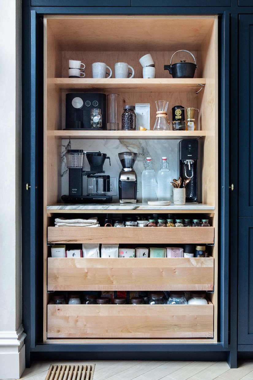 Coffee station made from natural wood inside dark cabinet with pocket doors.
