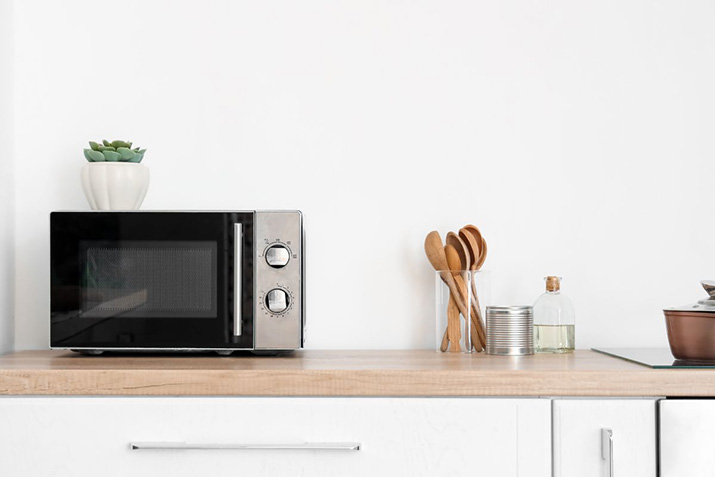 A silver microwave sitting on a plain wooden countertop.