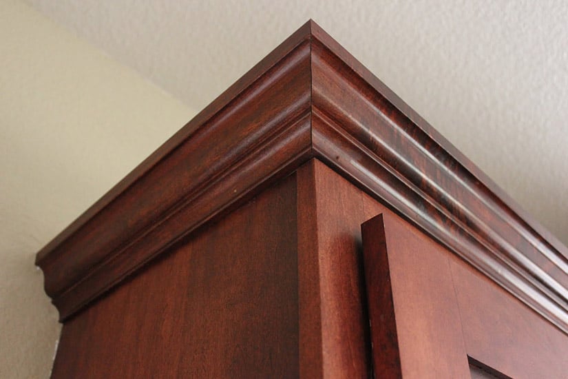 DIY crown molding final edge installation with dark wood cabinets.