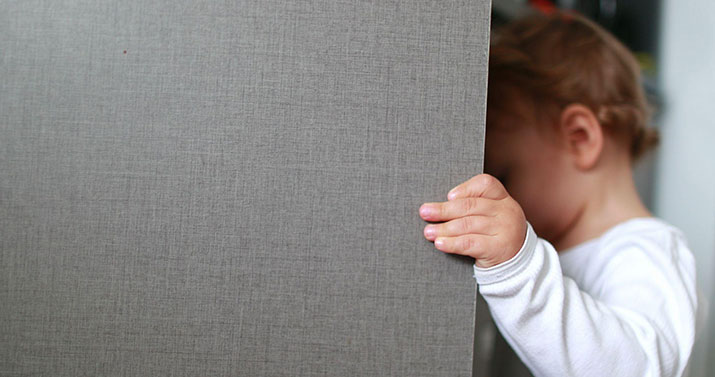 A little boy with a white shirt opening a grey cupboard door.