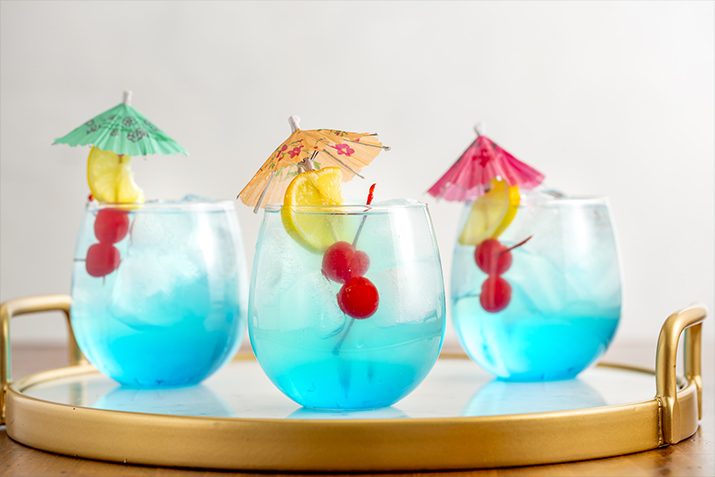 Mermaid Lemonade - Blue ombre cocktail garnished with cherries and lemon on an umbrella.