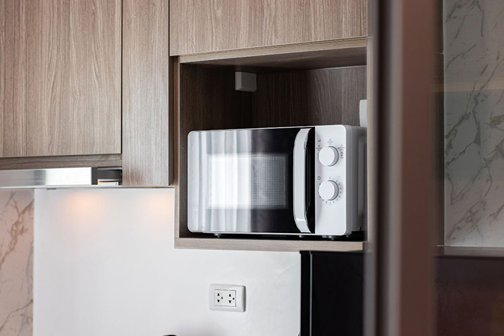 A white microwave among wood cabinets.
