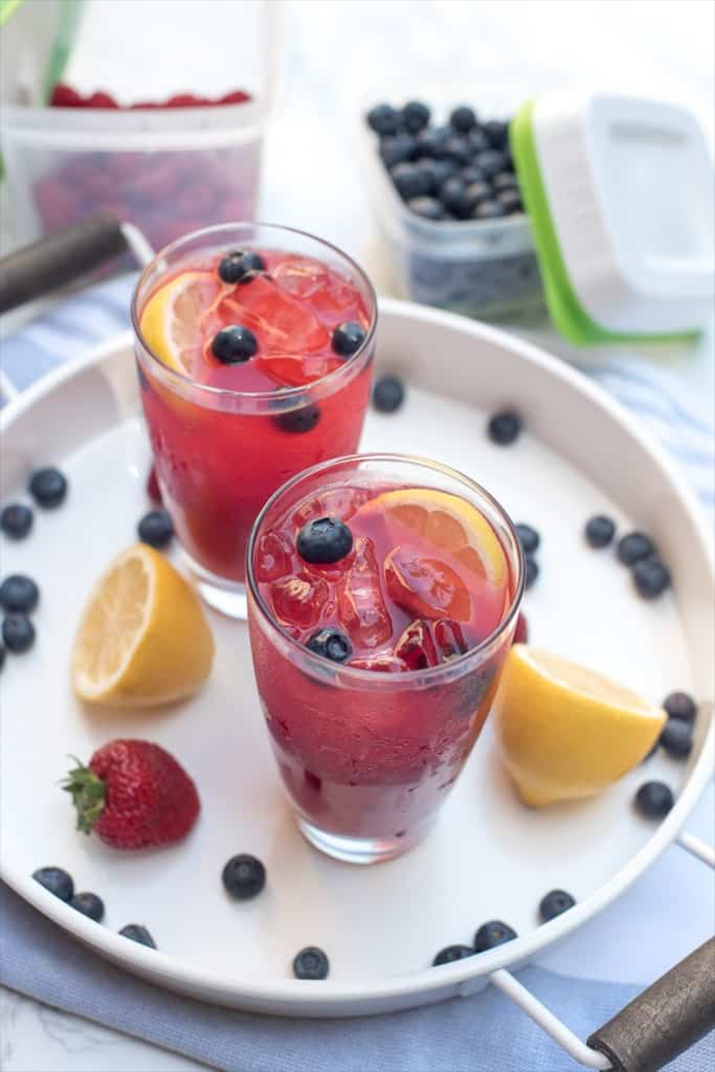Non Alcoholic Summer Berry Lemonade - Red summer berry lemonade served with blueberries, strawberries, and lemons as garnish.