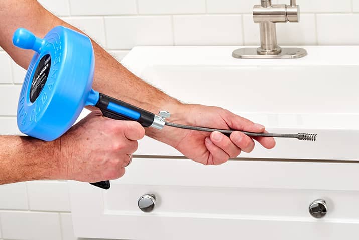 Person holding a handheld plumber's snake in front of clogged sink.