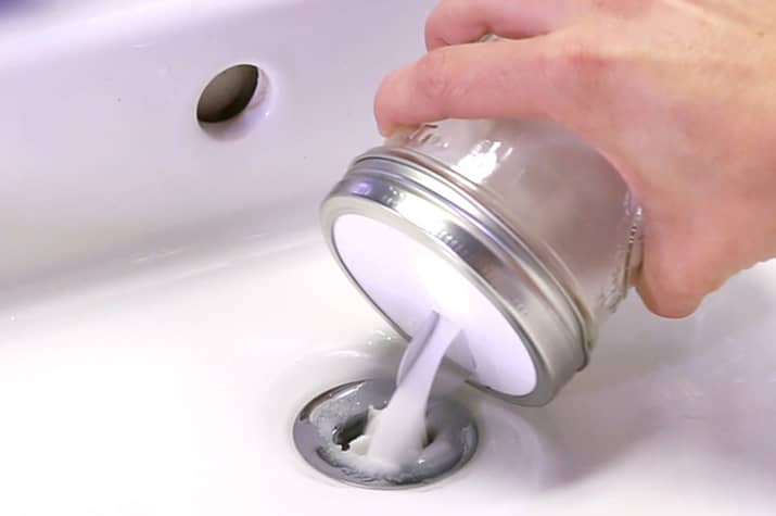 Pouring a mixture of baking soda and salt in sink drain.
