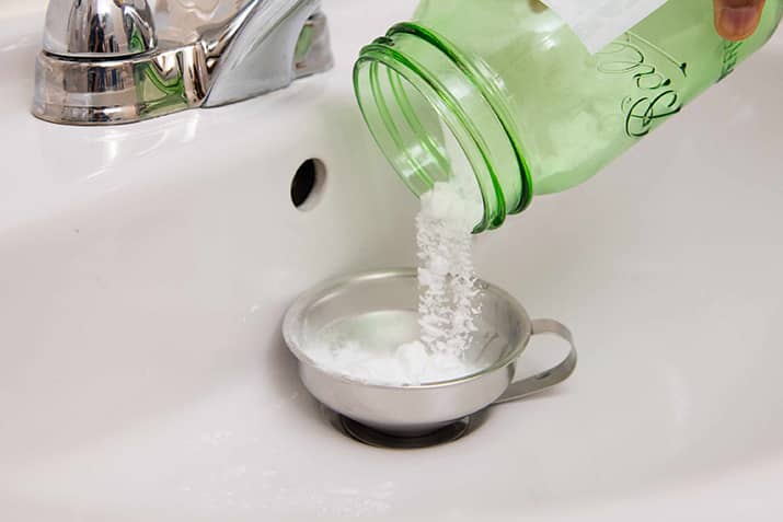 Pouring a mixture of baking soda and vinegar in sink drain.