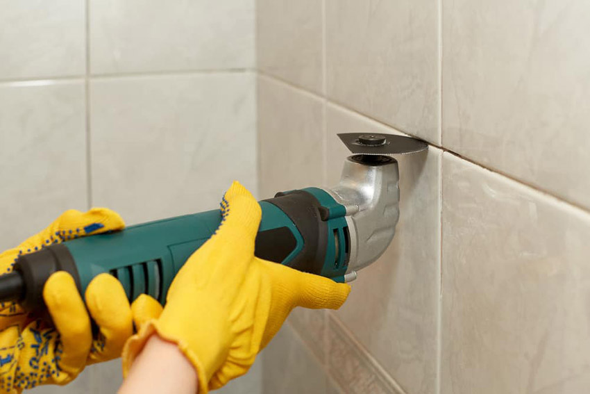 Homeowner using a grout remover to repair hairline crack in shower tile.