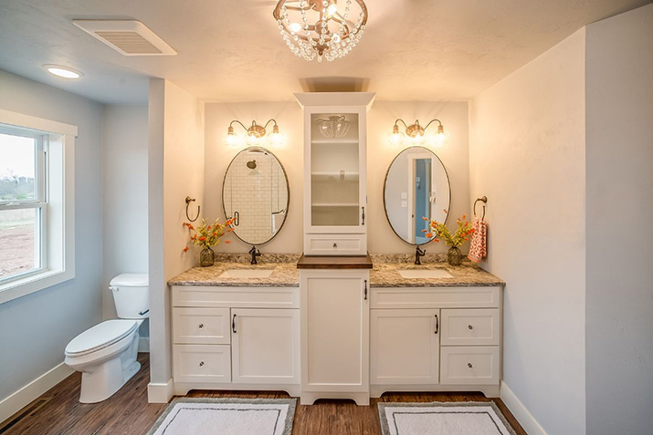White double-sink bathroom vanity with two mirrors, a central storage cabinet, and separate drawer and cabinet storage.